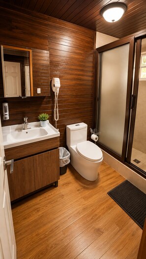 Bany modern amb panells de fusta, un lavabo blanc, un vàter i una dutxa amb portes de vidre gravat.