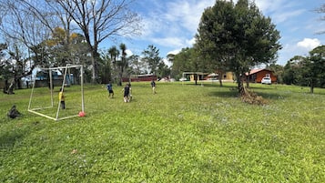 A grassy outdoor area with a soccer goal, trees, and a building in the background.