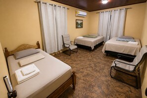 A room with two beds, a chair, a small table, and a painting on the wall.