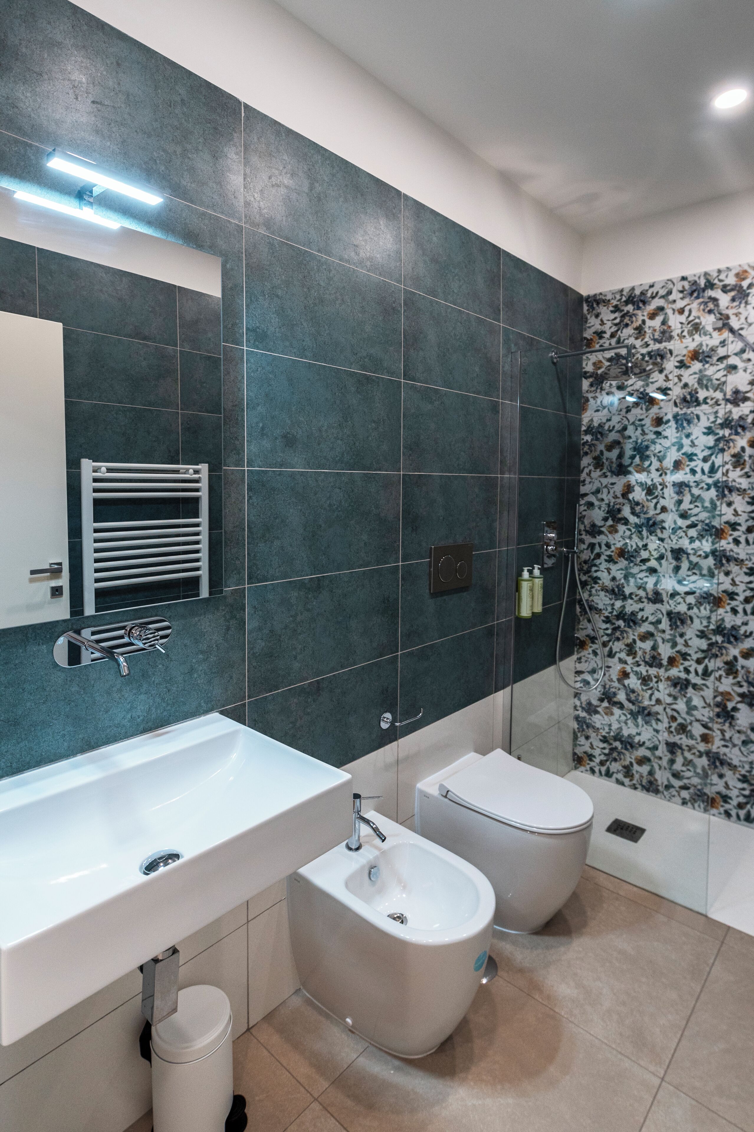 A modern bathroom with a large mirror, a white sink, two toilets, and a shower area.