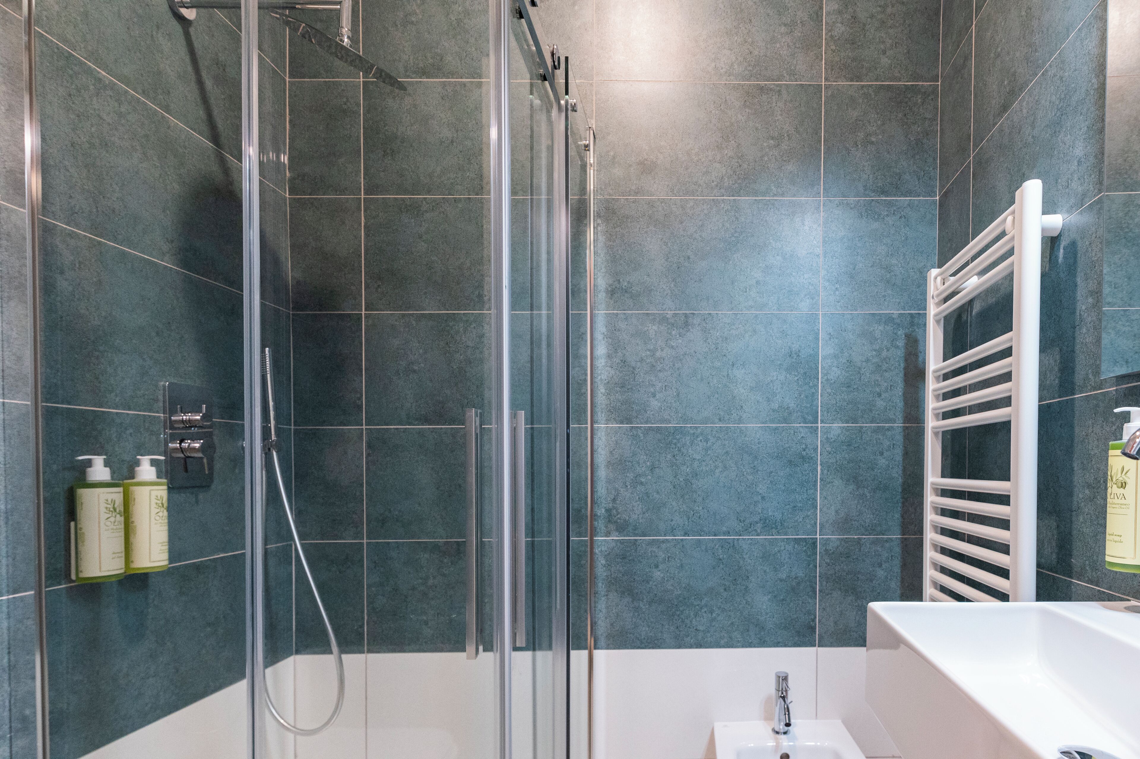 A modern bathroom with a glass-enclosed shower, a white sink, and a towel rack.