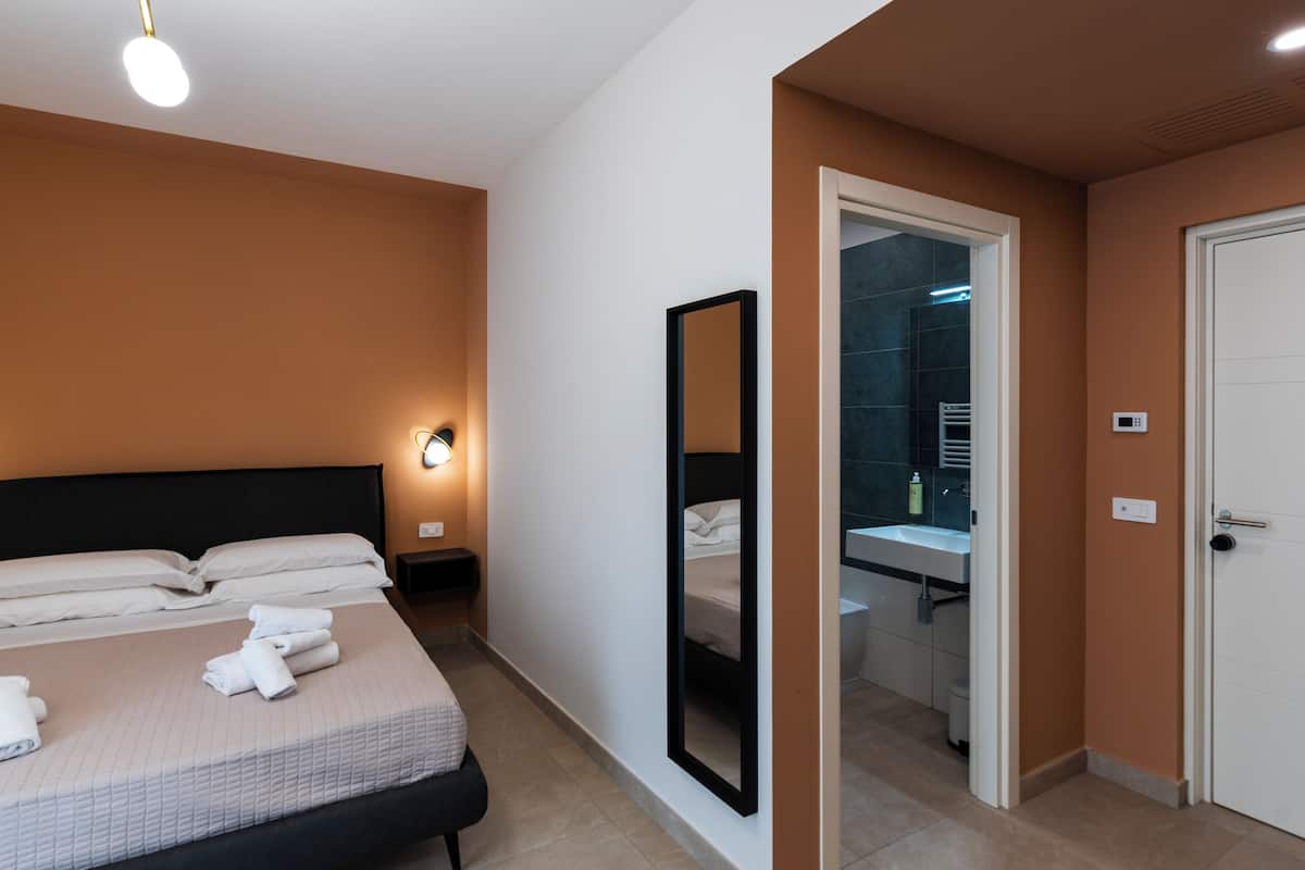 A hotel room with a bed, a nightstand, a mirror, a bathroom with a sink and a shower.