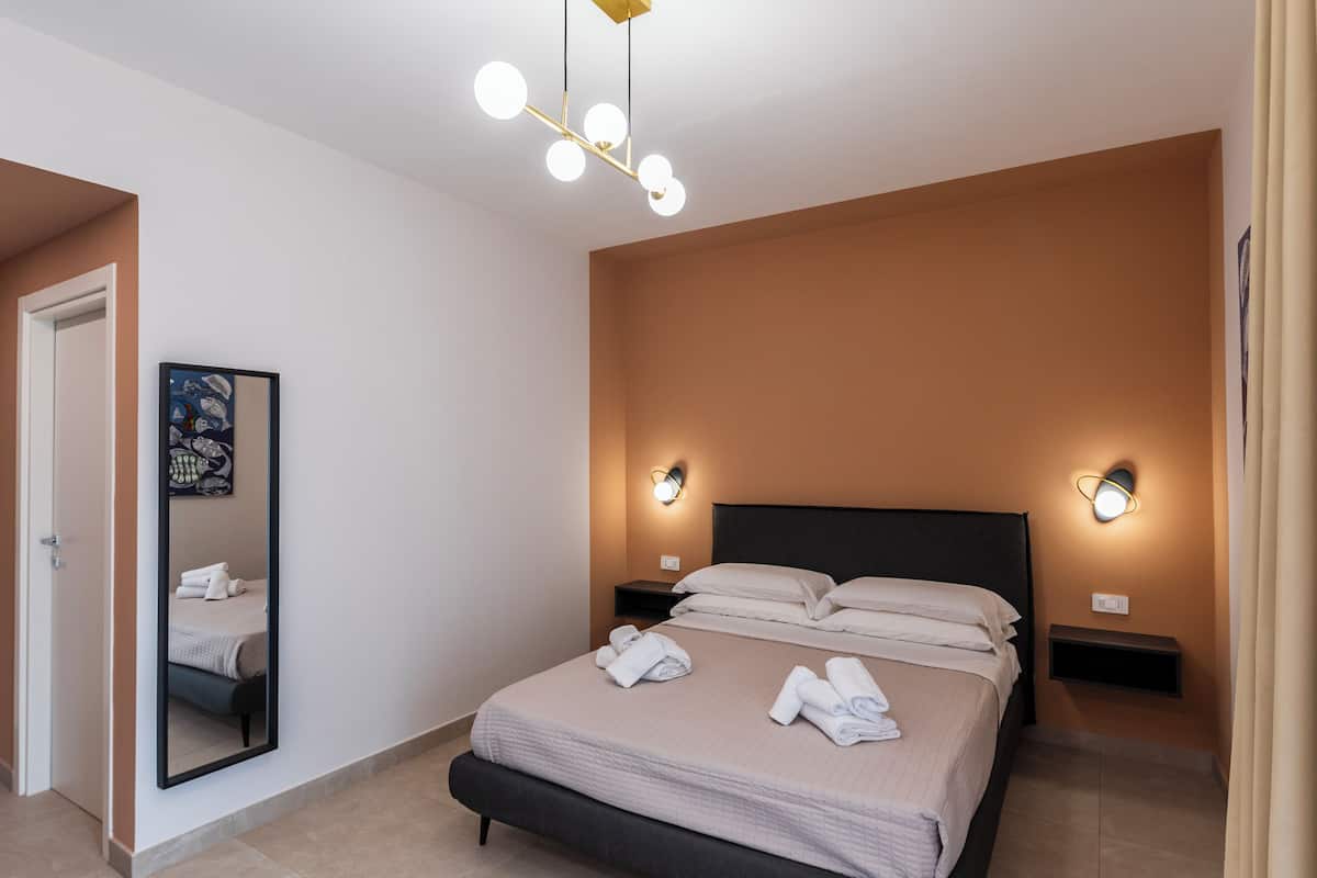 A hotel room with a bed, bedside tables, a wall-mounted light, a mirror, and a door.