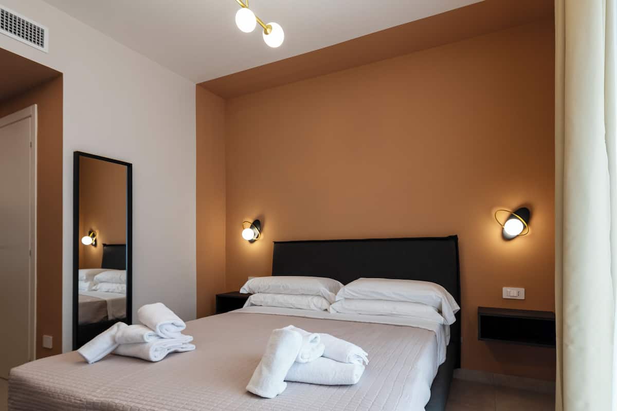 A hotel room with a bed, two bedside tables, a mirror, and wall-mounted lights.