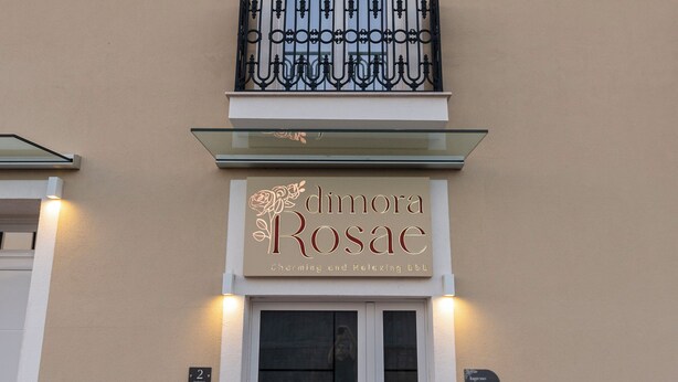 A building with a balcony, a sign reading 'Dimora Rosace,' and a door with a glass panel.