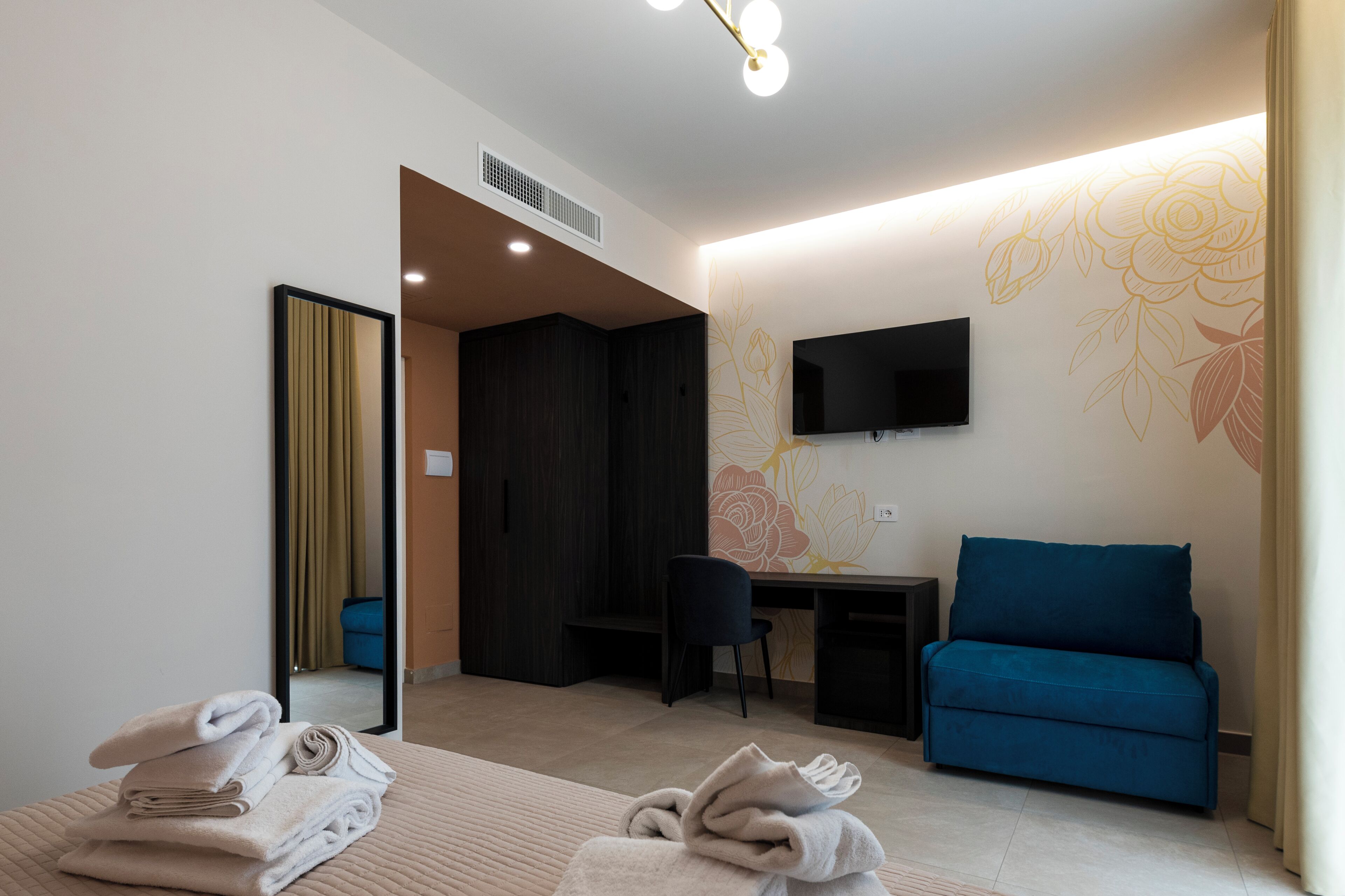 Une chambre d’hôtel moderne avec un lit, un bureau, un canapé bleu, une télévision et un miroir.