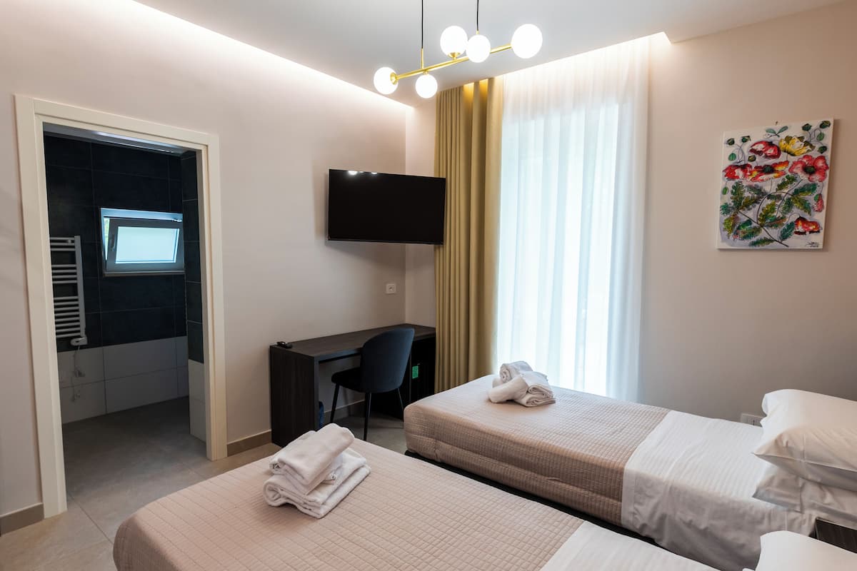 A hotel room with two beds, a desk, a TV, and a painting.