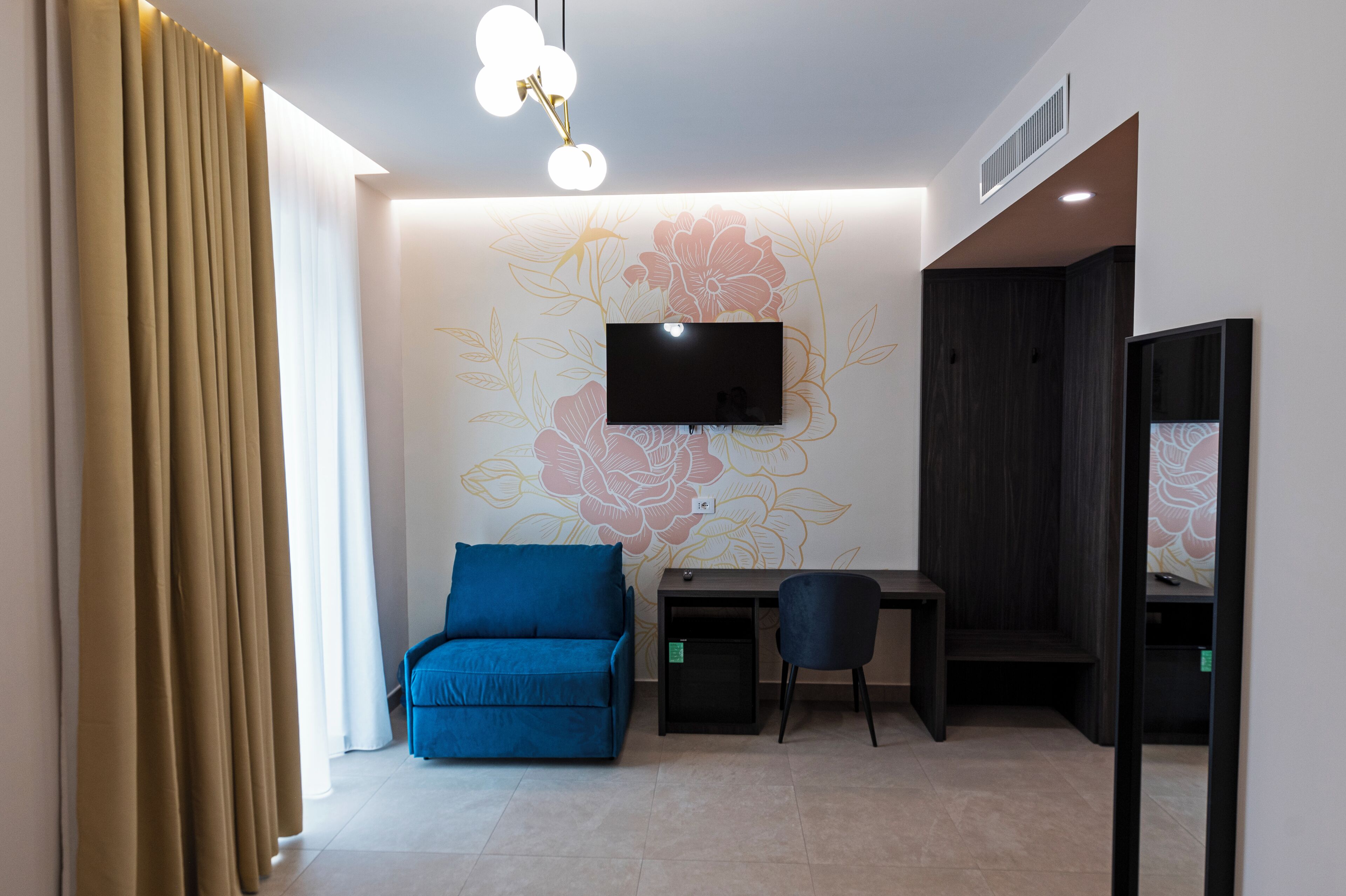 A room with a sofa, a desk, a chair, a TV, and a curtain.