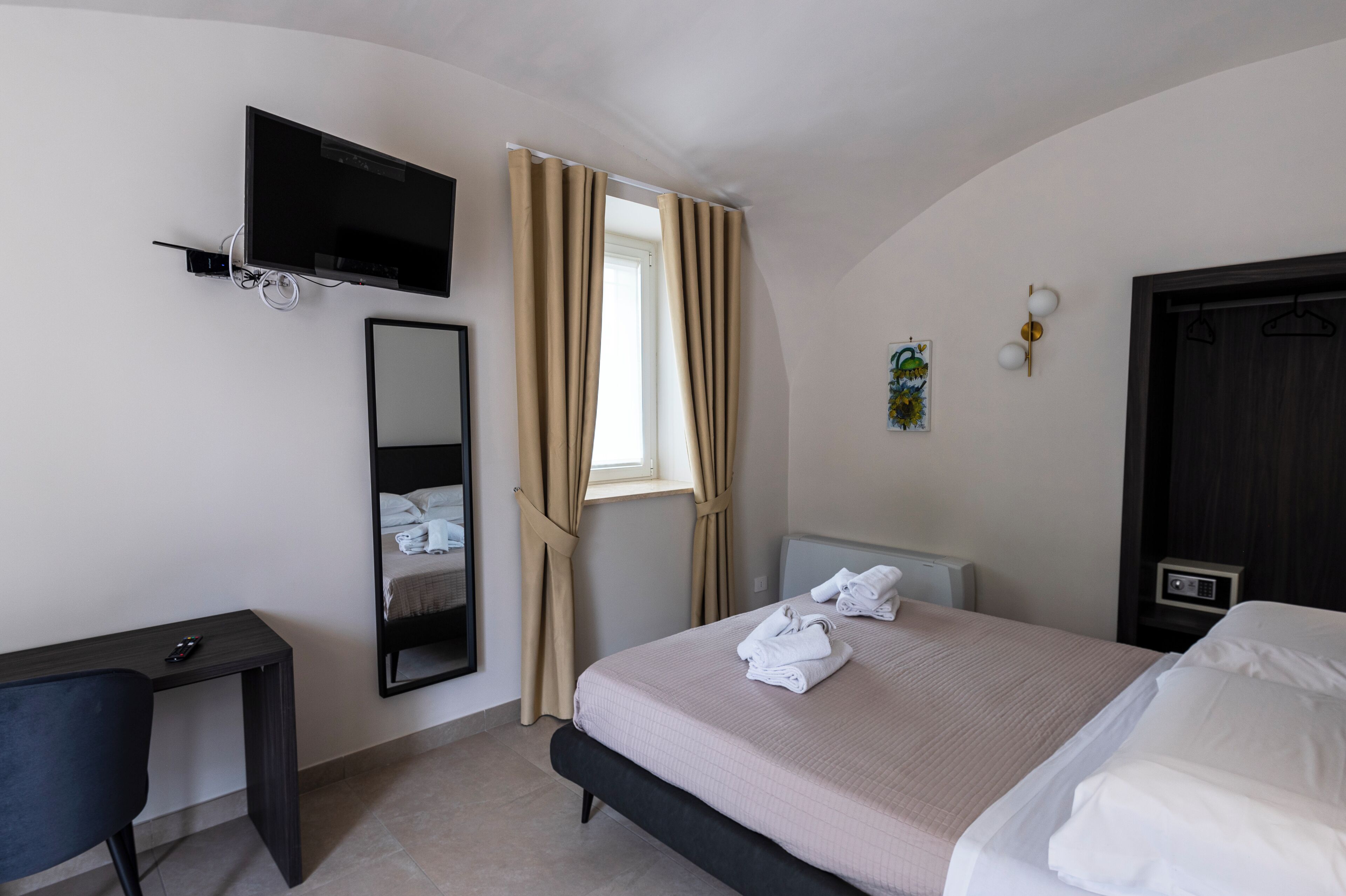Een hotelkamer met een bed, een bureau, een aan de muur bevestigde televisie, een raam met gordijnen en een deur.