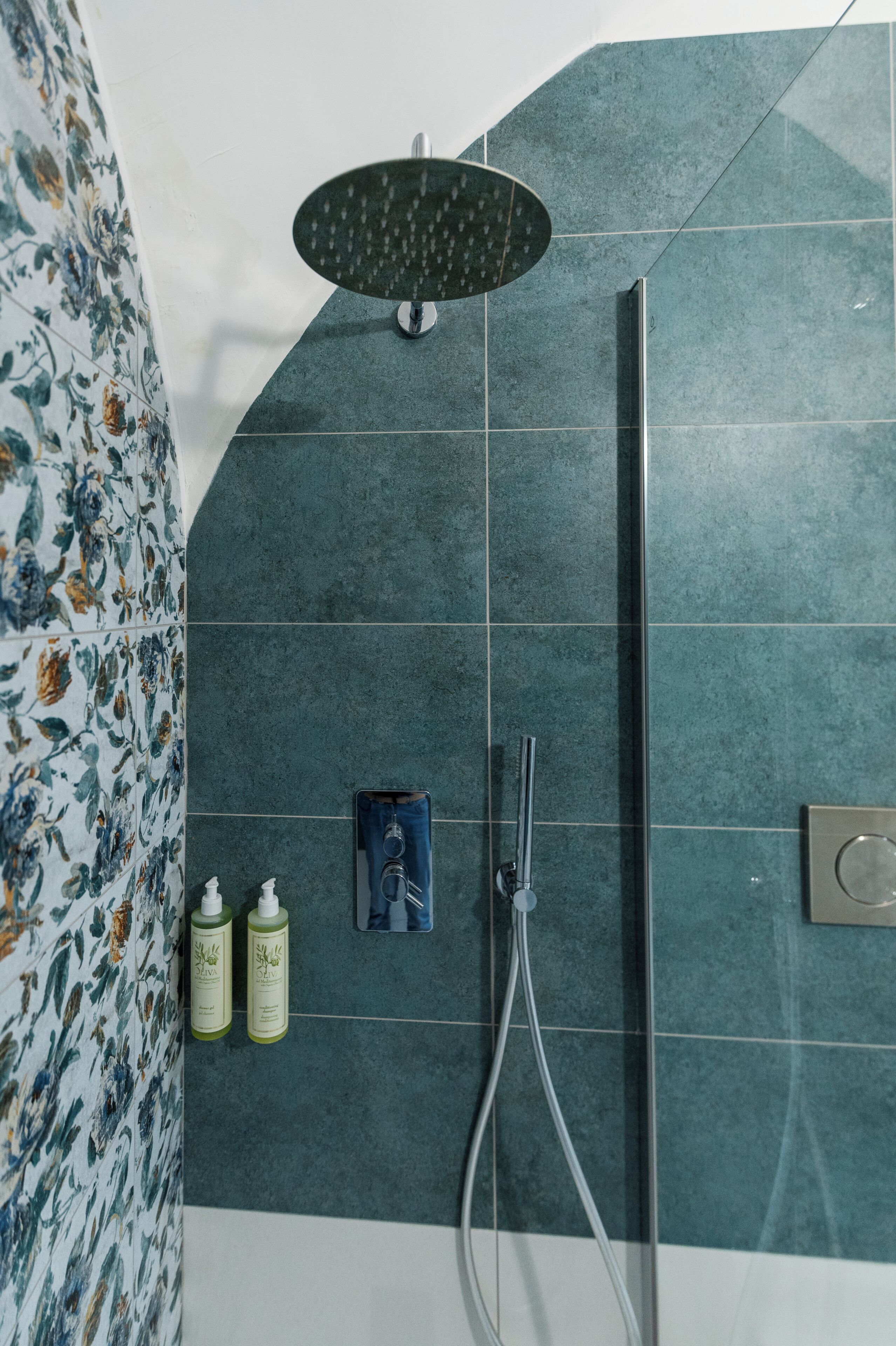 Een douchegedeelte met een regendouche, een handdouche en twee shampoo flessen.