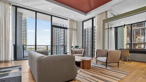Ein modernes Wohnzimmer mit einer Couch, Sesseln, einem Couchtisch und Blick auf die Stadt durch große Fenster.