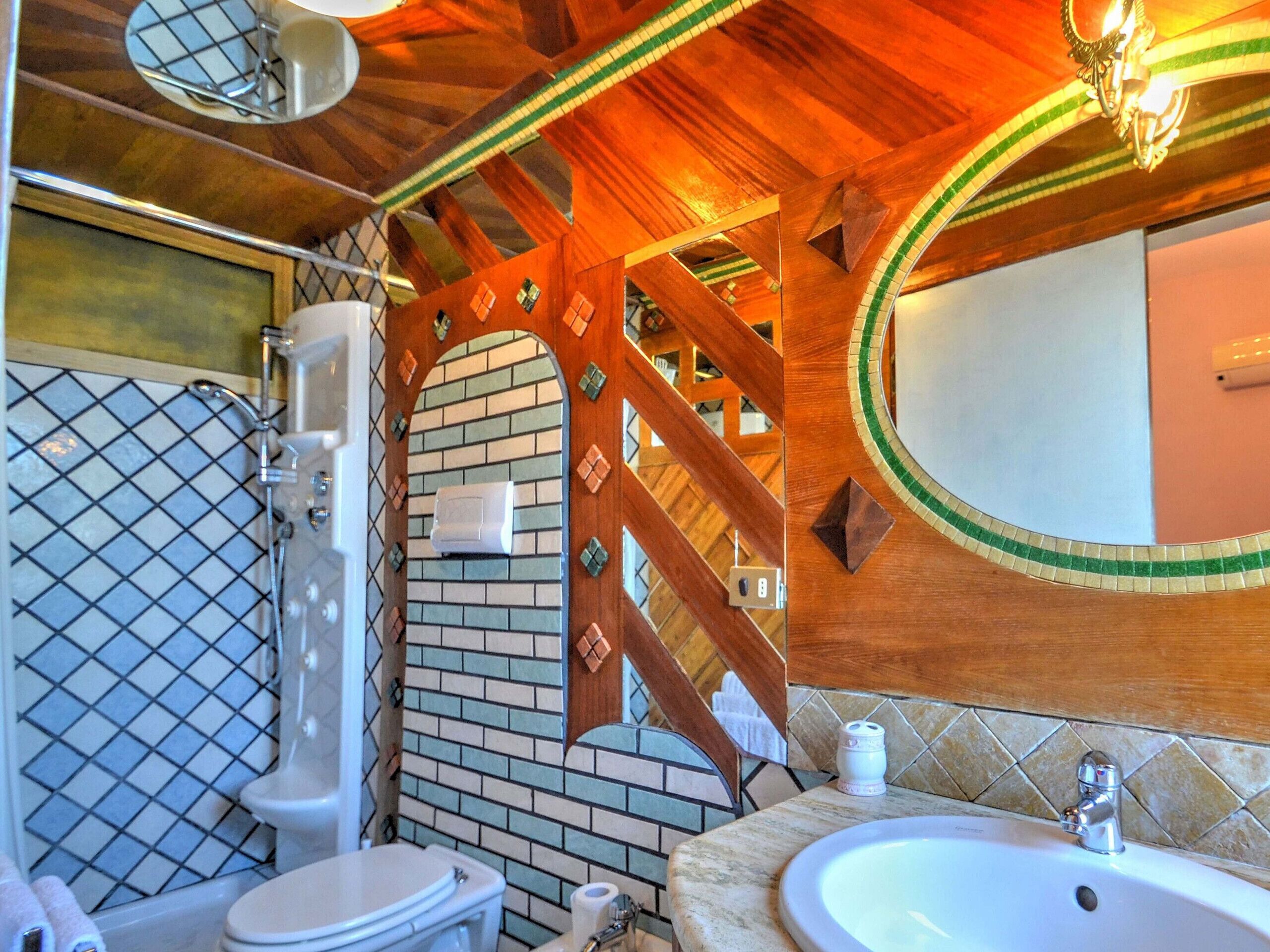 A bathroom with a wooden ceiling, a tiled wall, a mirror, a sink, and a toilet.