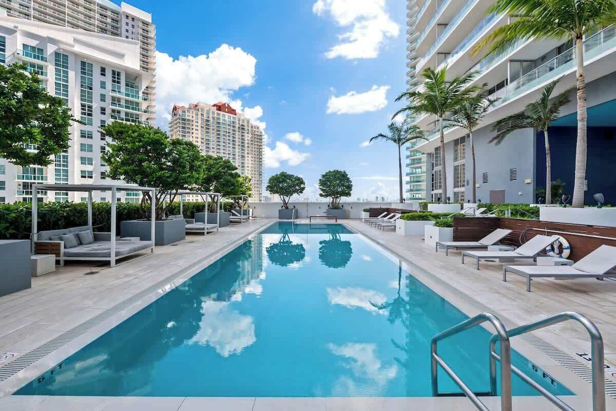 Ein moderner Hotelpoolbereich mit klarem, blauem Wasser, Liegestühlen und Palmen.