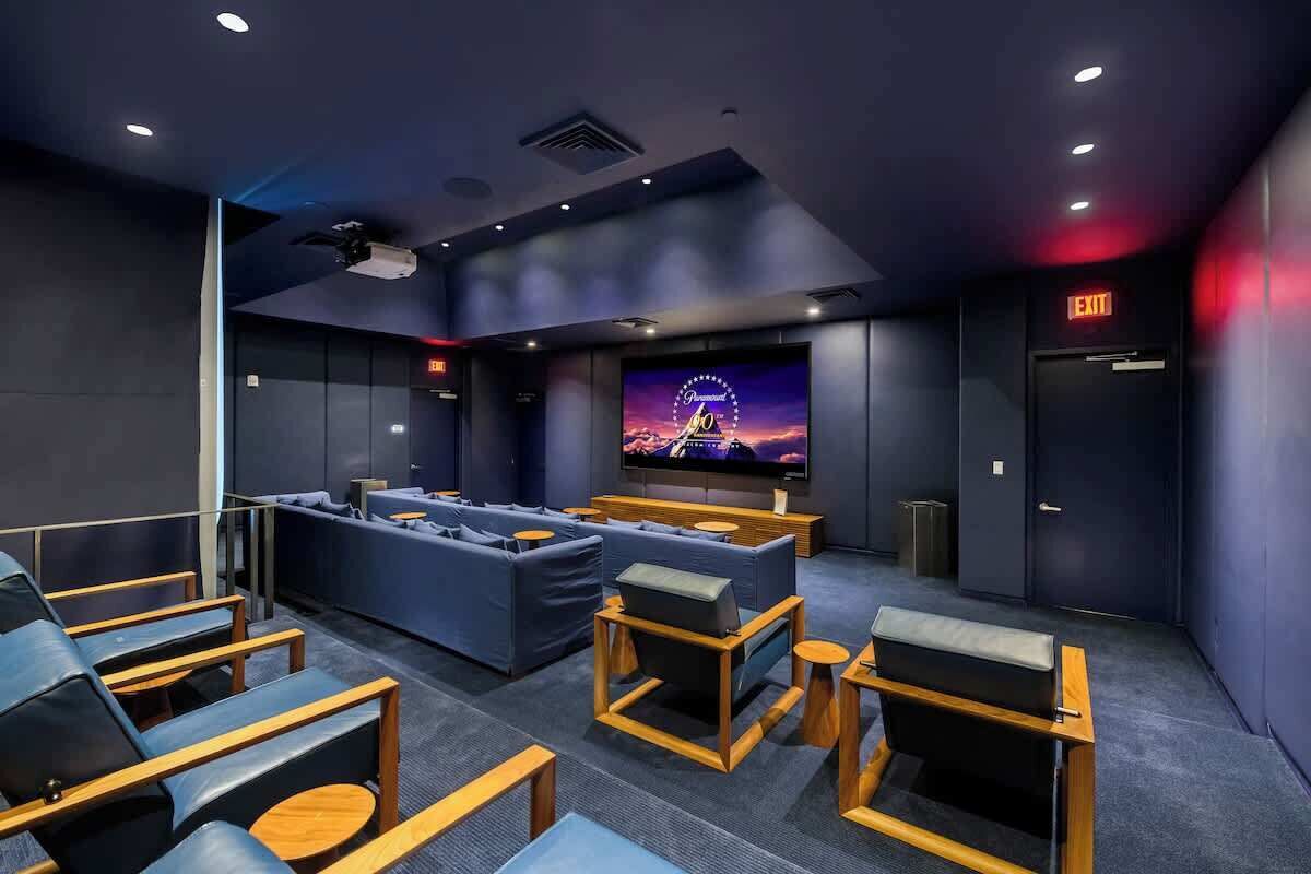 Una sala de cine moderna con una pantalla grande, asientos cómodos y una decoración en tonos oscuros.