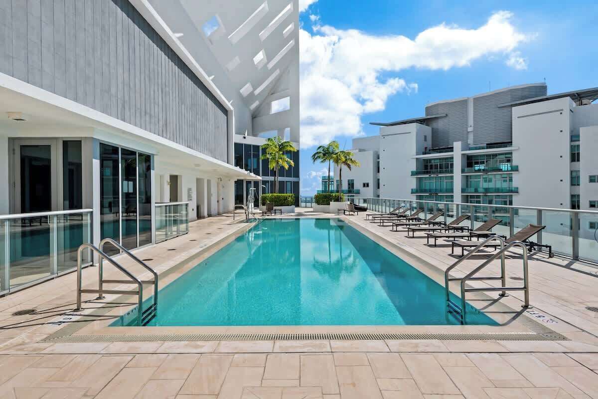 Un hotel moderno con piscina centrale, ringhiere in vetro e una vista aperta sul cielo.