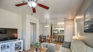 A living room with a TV, a ceiling fan, a dining area with a table and chairs, and a kitchen in the background. - Modern 2BR Condo w/ Pool & Parking in Scottsdale (Scottsdale)