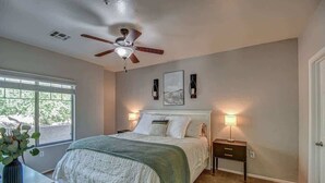 A bedroom with a bed, a ceiling fan, a window, and a nightstand with a lamp. - Modern 2BR Condo w/ Pool & Parking in Scottsdale (Scottsdale)