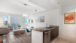 Un appartement moderne doté d’un îlot de cuisine, d’un coin repas et d’une grande fenêtre offrant une vue sur la ville.