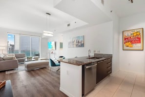 A modern apartment with a kitchen island, dining area, and a large window offering a city view. - 47th-Floor Brickell Condo w/ City Views & Pool (Miami)