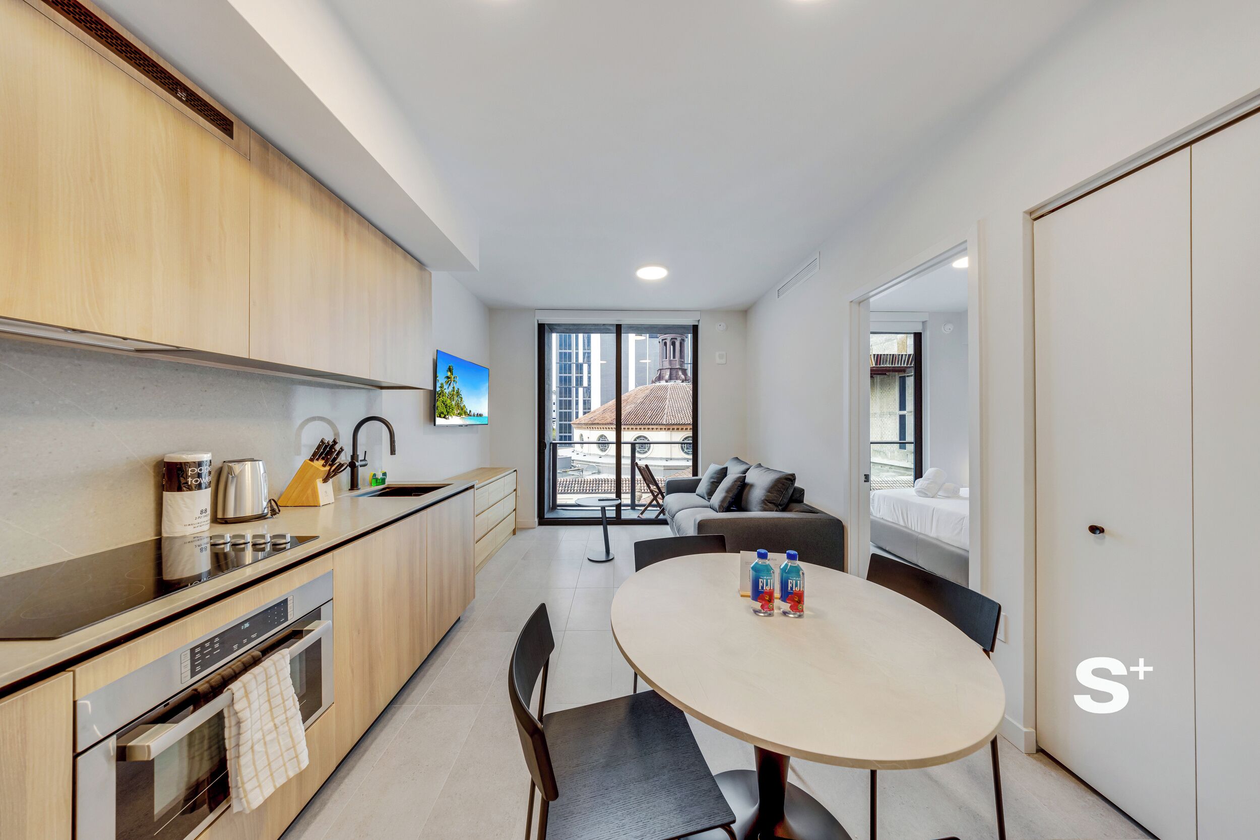 A modern kitchen with a dining area, a sofa, and a view of the outside.