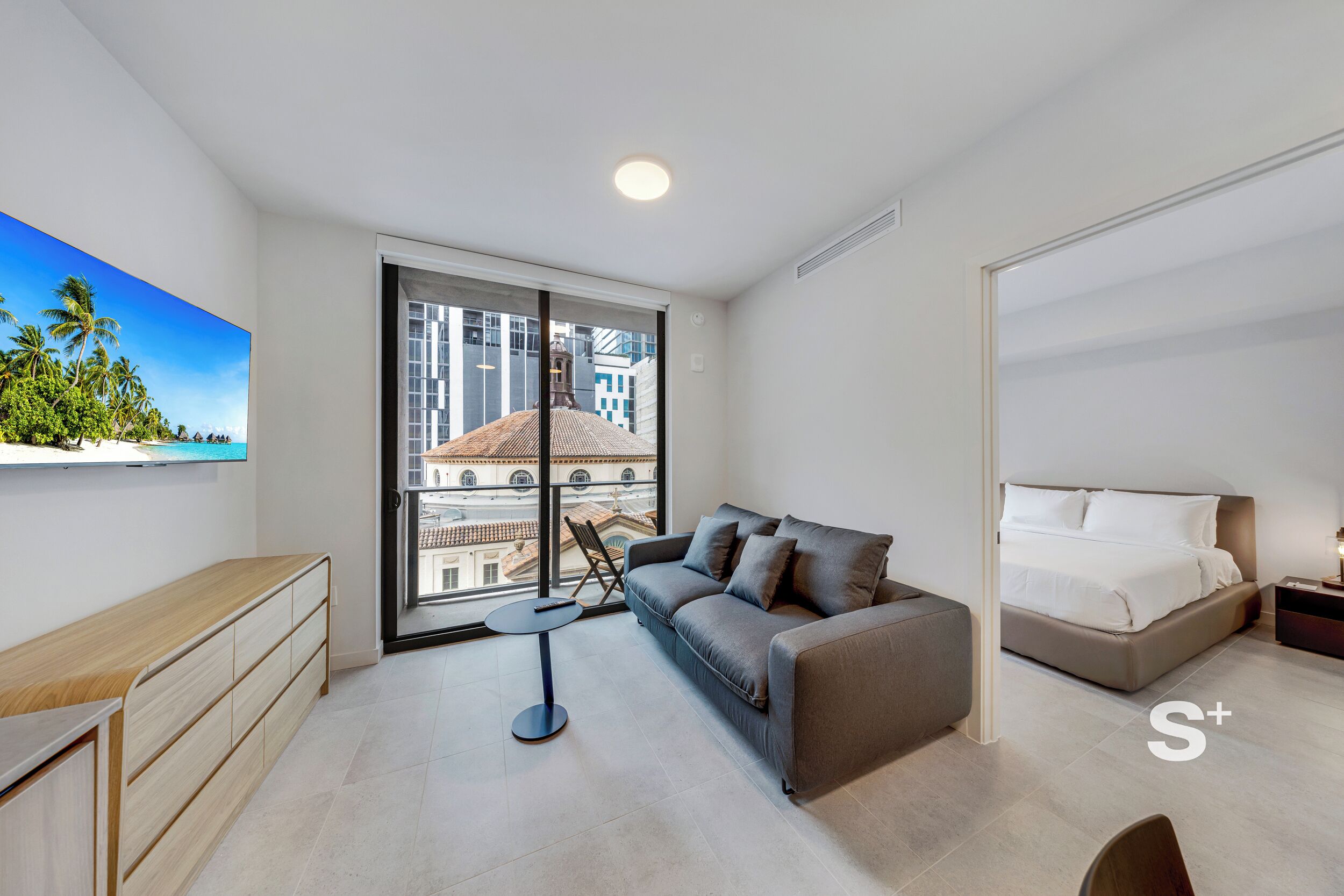 A modern bedroom with a large window, a sofa, a bed, and a desk.