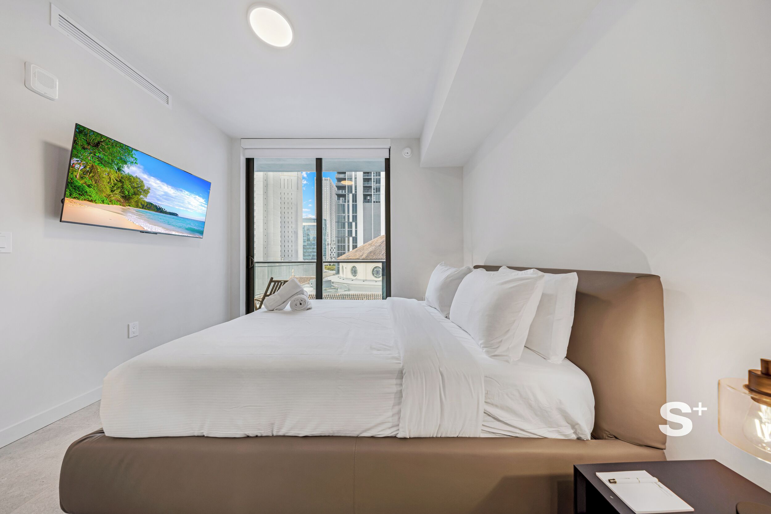 Een moderne slaapkamer met een groot bed, een televisie aan de muur en uitzicht op de stad door het raam.