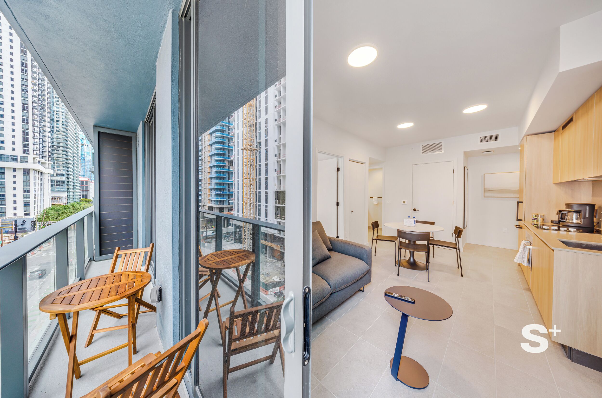 Um apartamento moderno com varanda, sala de estar com sofá e mesa de jantar, e cozinha com armários de madeira.