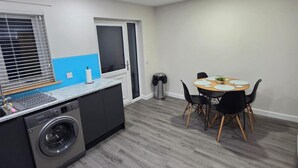 A compact kitchen with a washing machine, a sink, and a dining area with a round table and chairs. - 2 Bed House Sleeps 5 -private Garden (Stirling)