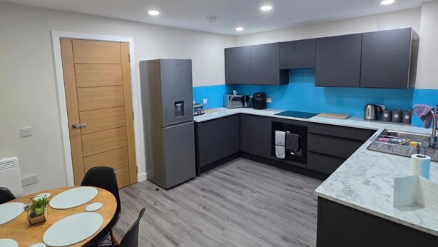 A modern kitchen with dark cabinets, a stainless steel refrigerator, and a blue backsplash. - 2 Bed House Sleeps 5 -private Garden (Stirling)