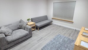 A modern living room with a grey patterned sofa, a grey couch, a small wooden side table with a plant, and a grey rug. - 2 Bed House Sleeps 5 -private Garden (Stirling)