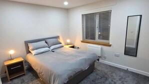 A bedroom with a bed, bedside tables, a radiator, a window with blinds, and a mirror on the wall. - 2 Bed House Sleeps 5 -private Garden (Stirling)
