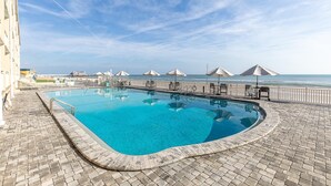 A swimming pool with a brick border, beach umbrellas, and a view of the ocean. - Daytona Inn Beach Resort 409 (Daytona Beach)