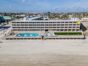 A multi-story hotel with a rooftop pool area and a large building in the background. - Daytona Inn Beach Resort 409 (Daytona Beach)
