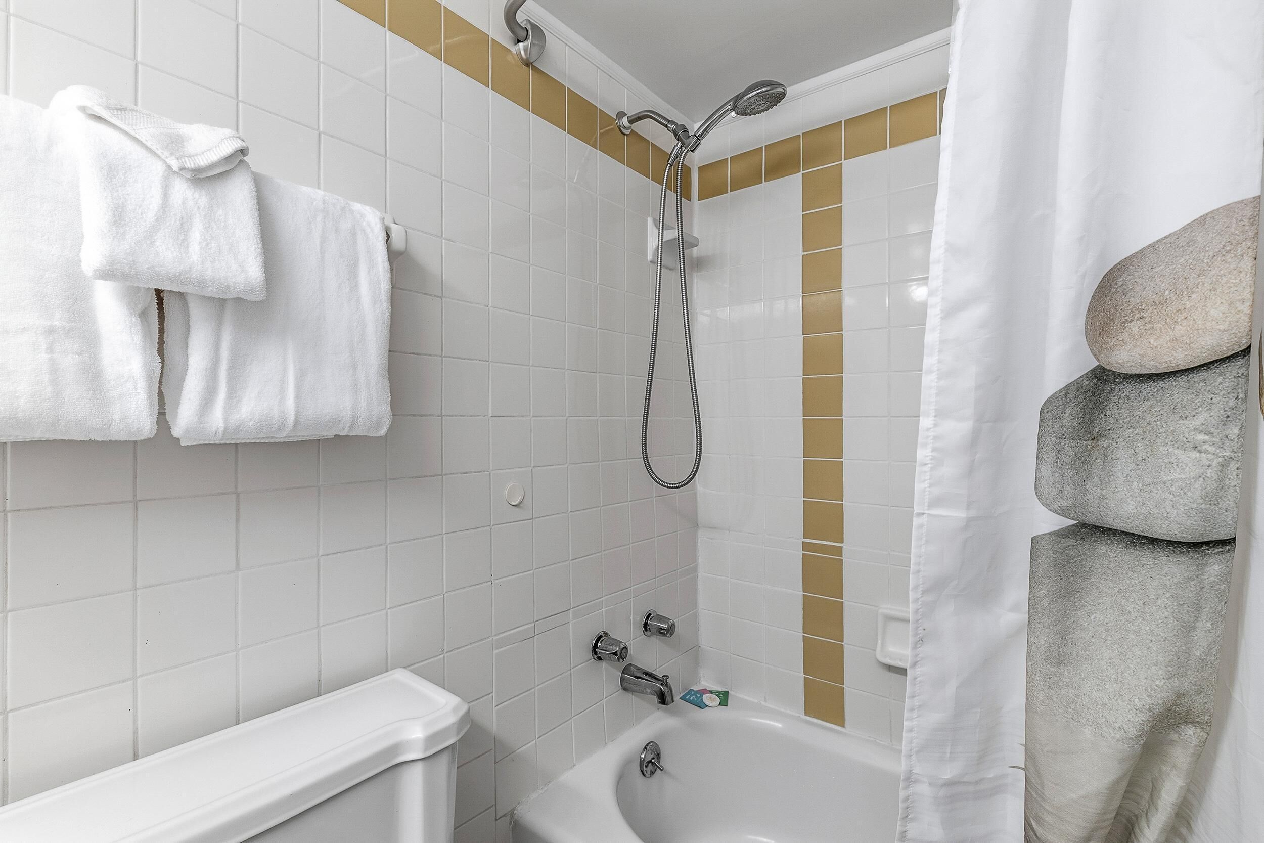 A bathroom with white tiled walls, a bathtub, a shower with a handheld showerhead, and a towel rack with two towels.