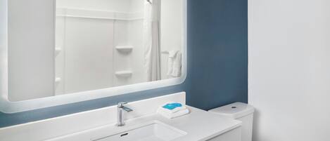 Un baño con lavamanos blanco, un espejo, ducha e inodoro.
