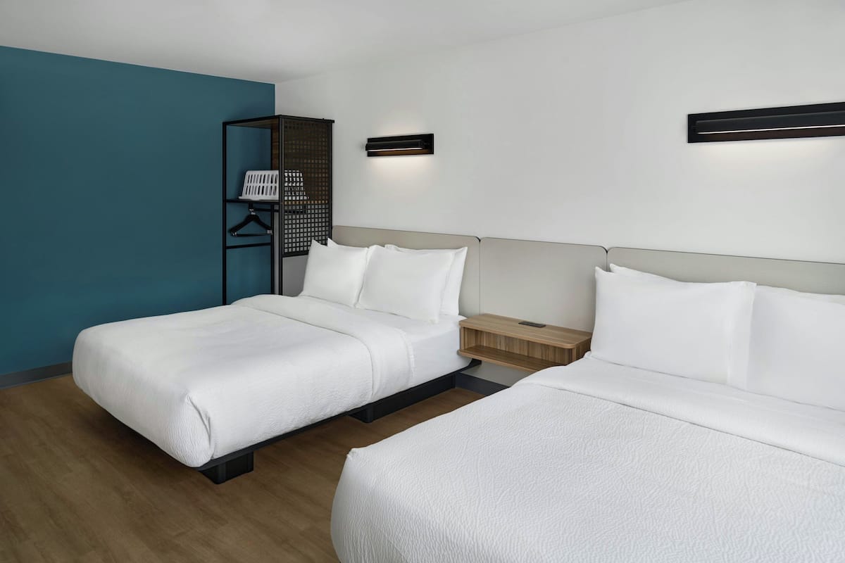 Een hotelkamer met twee bedden, een houten vloer, een wand in turquoise kleur en een wandplank met een wasmand.
