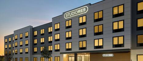 A modern hotel building with a 'STUDIORES' sign, multiple windows, and a parking lot with handicapped parking spaces.