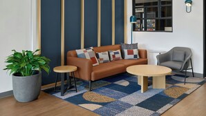 Un salon moderne comprenant un canapé, deux tables d’appoint, un fauteuil gris, une grande plante en pot et un tapis à motifs.
