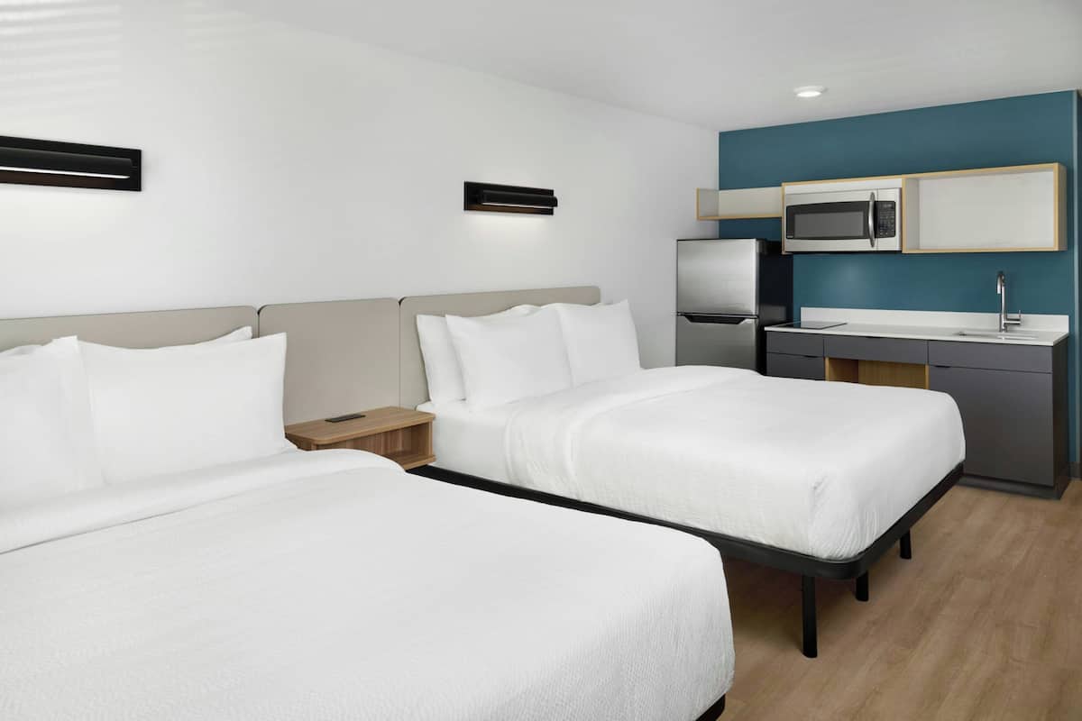 A hotel room with two beds, a kitchenette, and a small bedside table.
