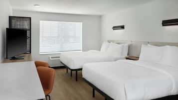 A hotel room with two beds, a desk, a TV, and a window with blinds.