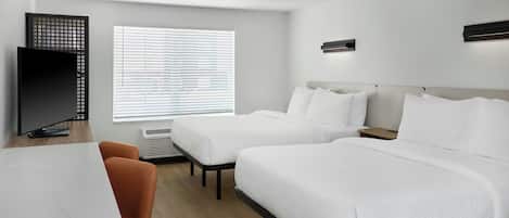 Ein Hotelzimmer mit zwei Betten, einem Schreibtisch, einem Fernseher und einem Fenster mit Jalousien.