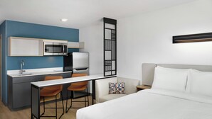 Une chambre d’hôtel de taille réduite, équipée d’une kitchenette, d’un lit, d’un bureau et d’une chaise.