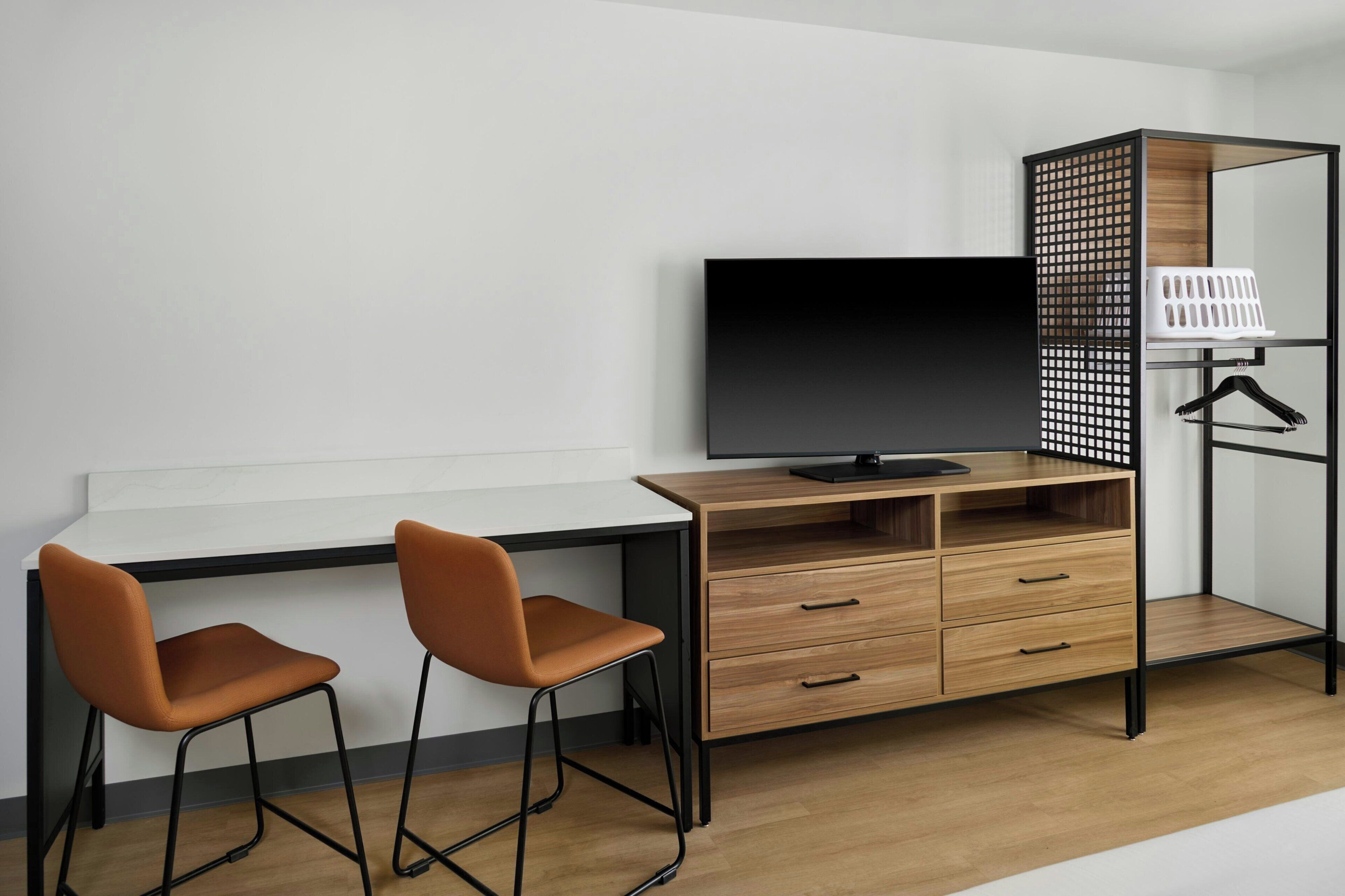 A modern room with a wooden desk, two chairs, a TV, and a mirrored wardrobe with a hanging rack.