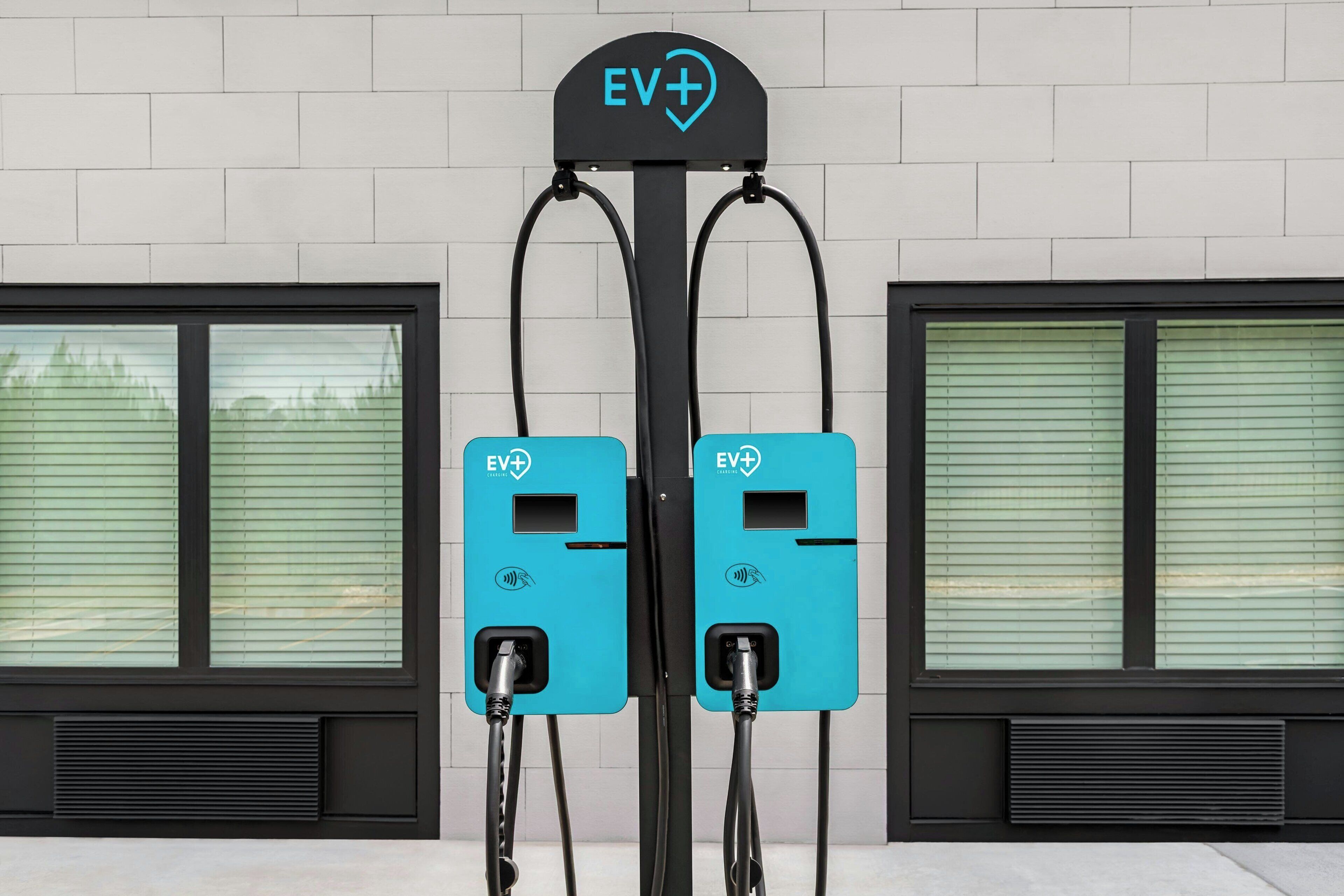 Två laddstationer för elfordon, med en skylt ovanför, monterade på en vägg med fönster.