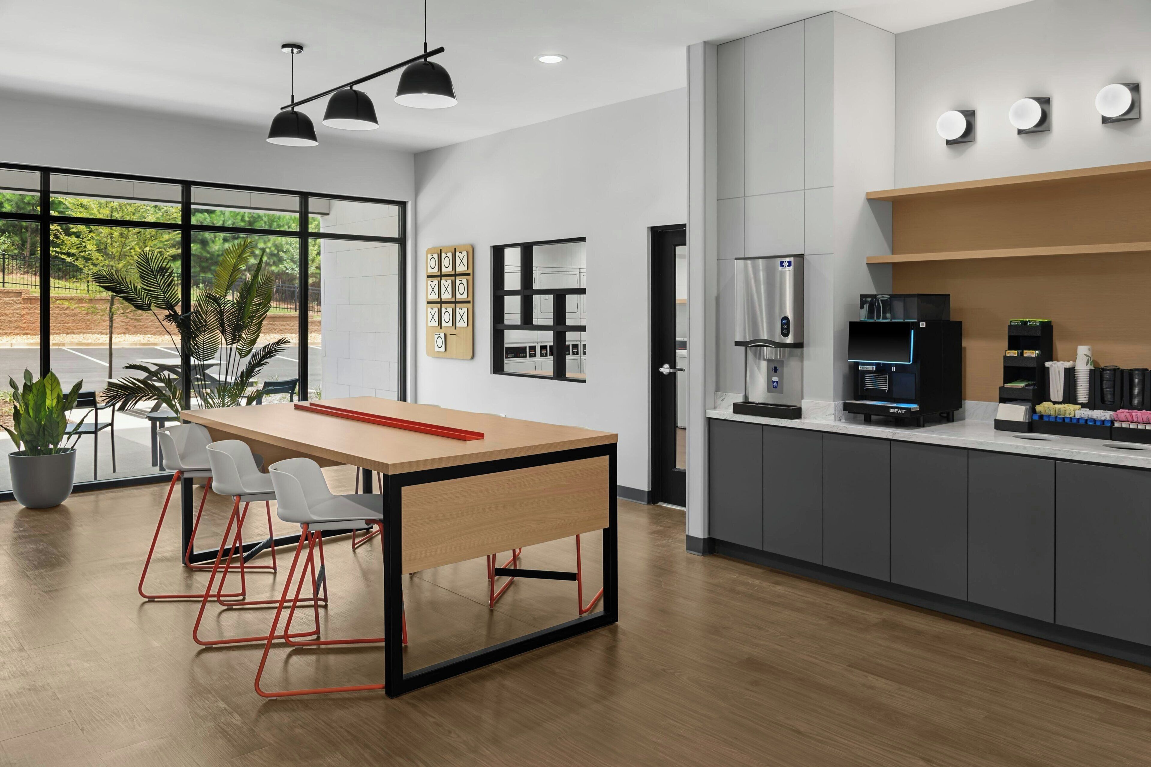 A modern kitchen with a wooden table, bar stools, a coffee machine, and a view of the outdoors.