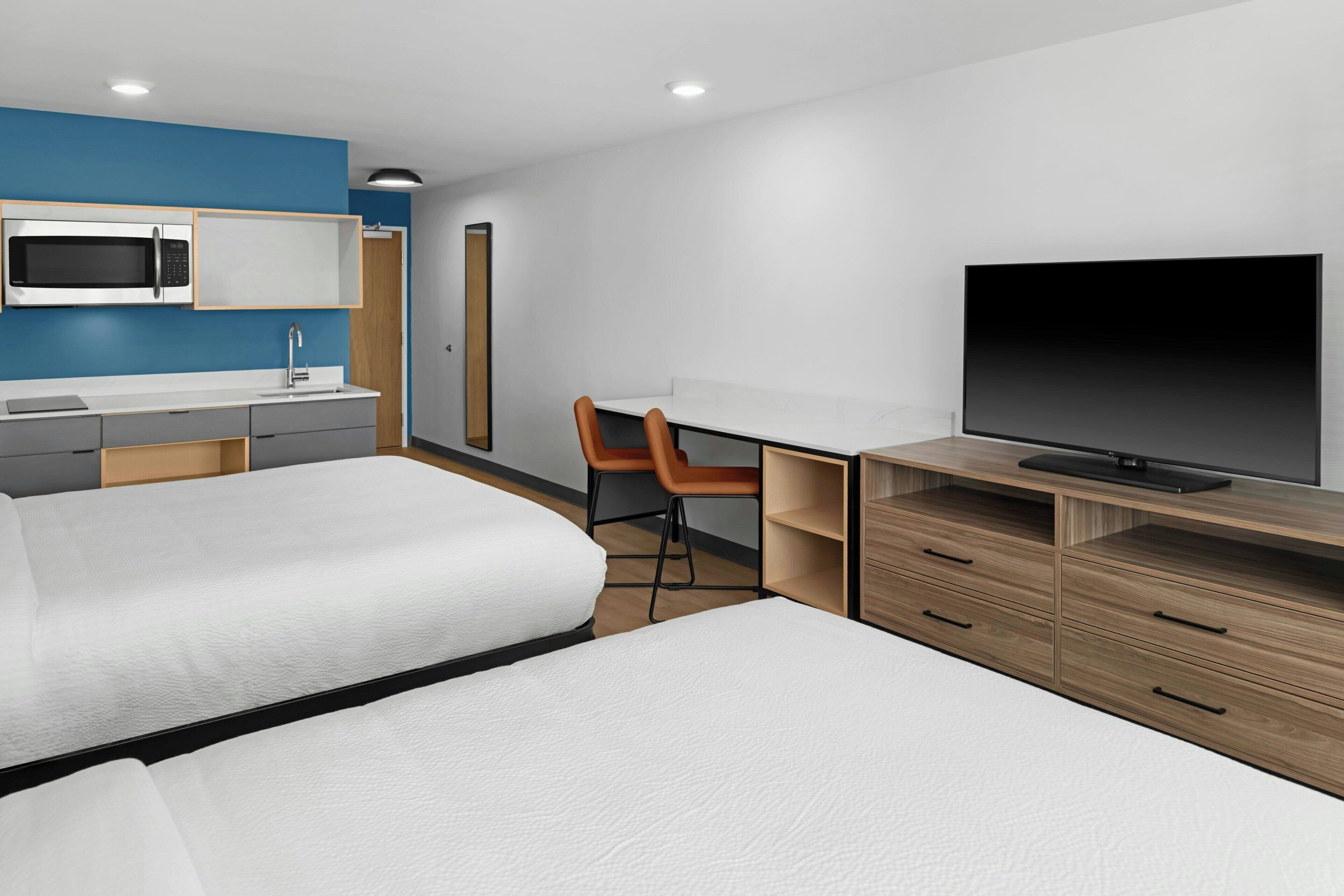 A hotel room with two beds, a desk, a chair, a TV, a microwave, and a small bathroom.