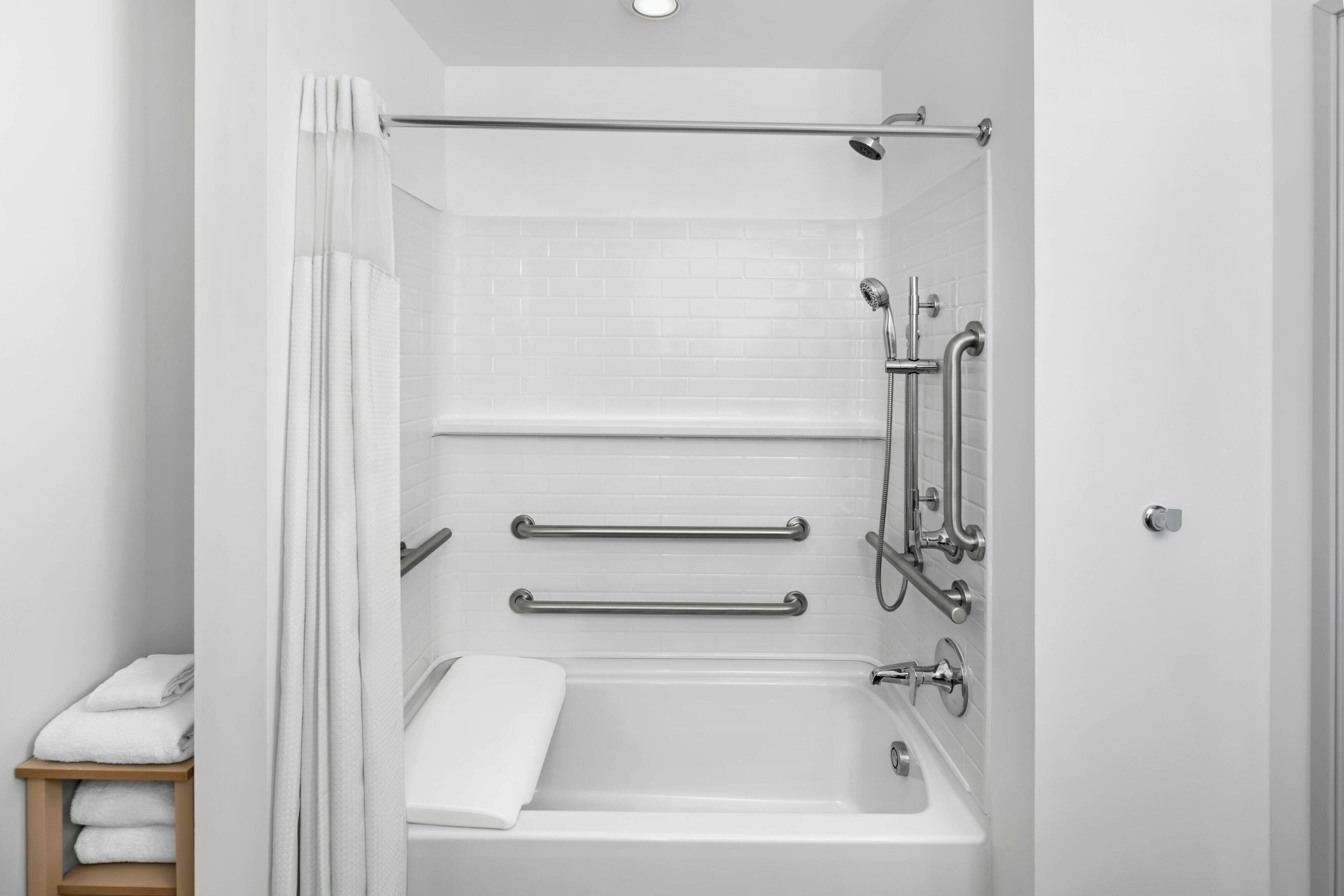 Un baño moderno con ducha a ras de suelo, barras de apoyo y pared de azulejos blancos.
