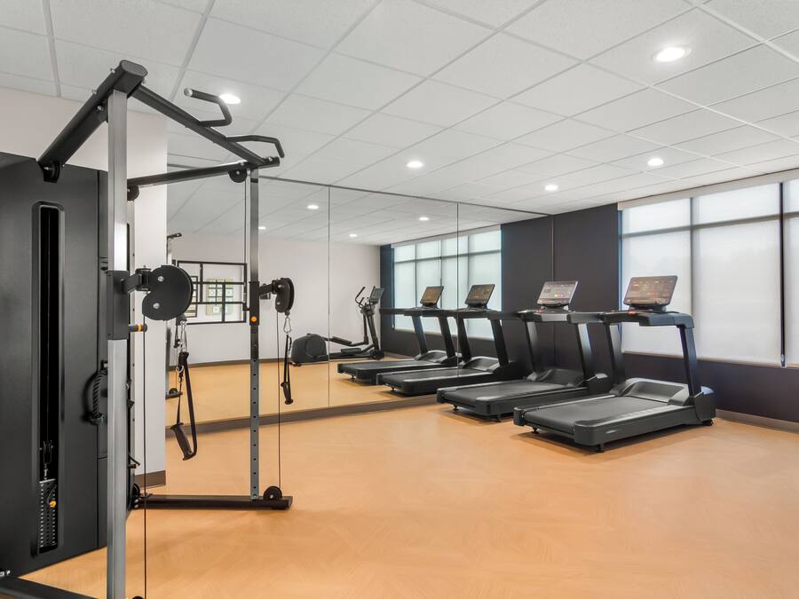 Un gimnasio con cintas de correr, una máquina de pesas y un espejo.