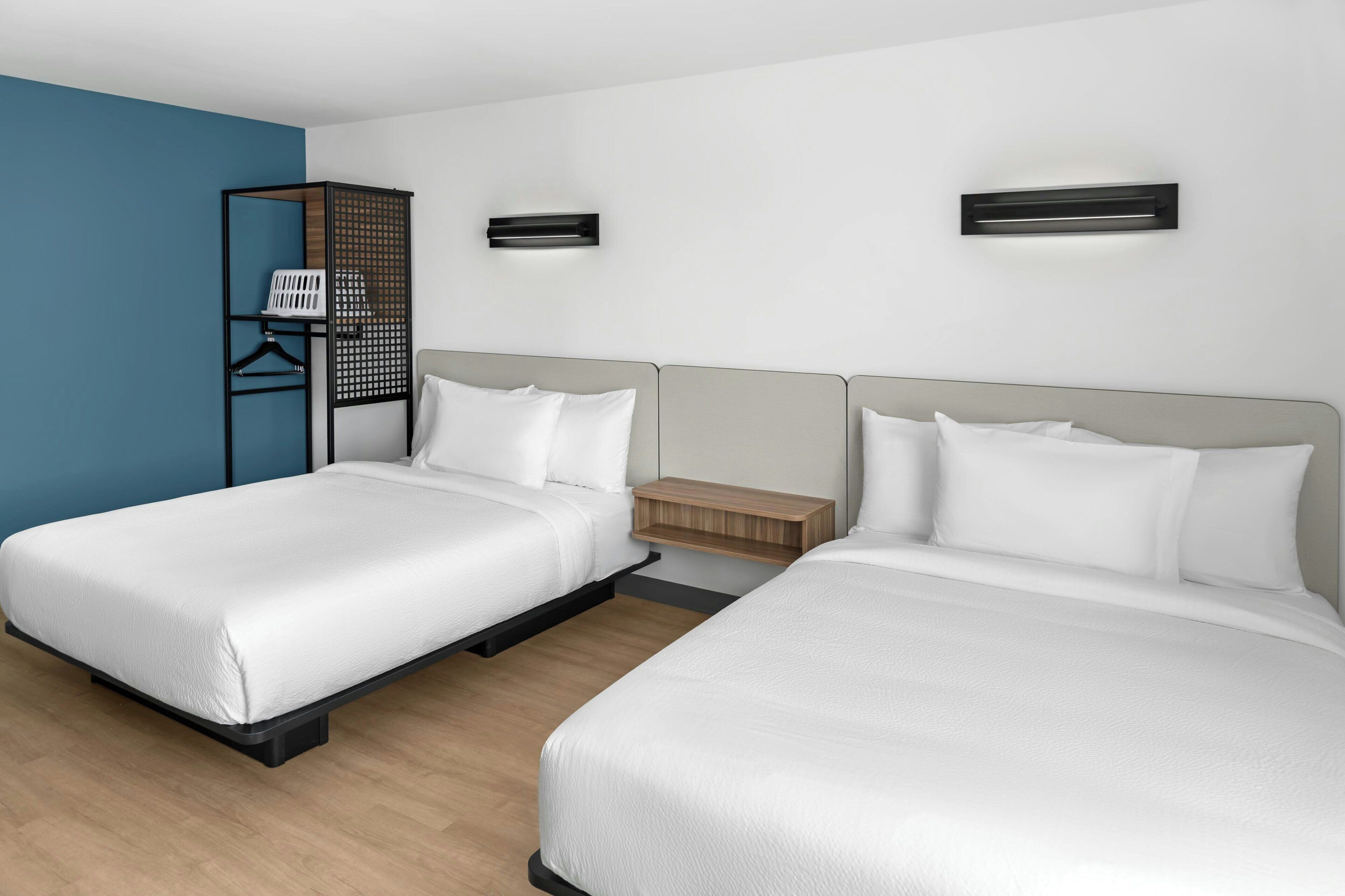 Habitación de hotel con dos camas, una mesita de noche de madera, aire acondicionado montado en la pared y una pared de acento azul.
