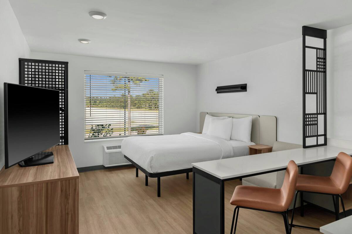 Een moderne hotelkamer met een bed, bureau, televisie en zithoek.